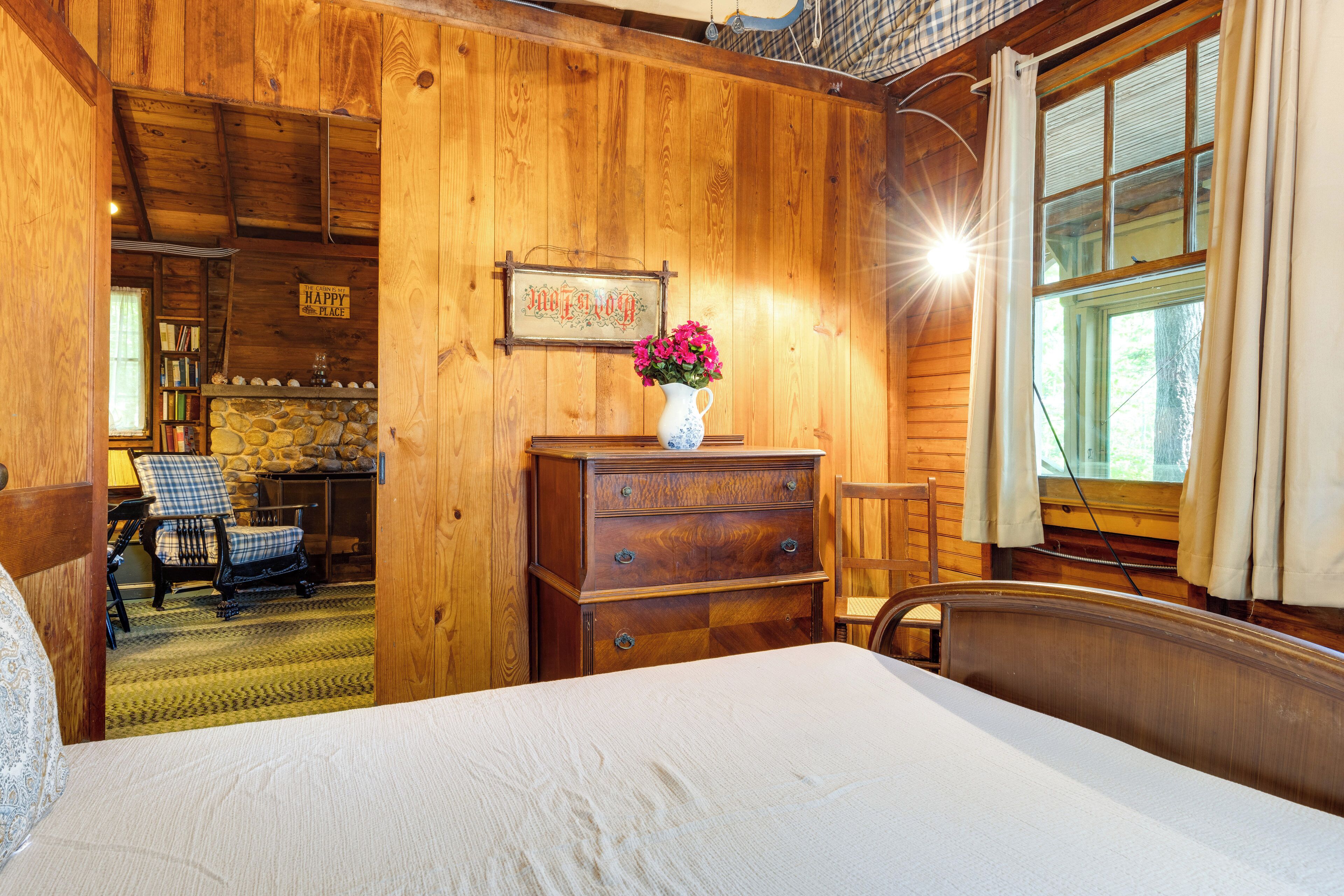 A wooden room with a bed, a dresser, a chair, and a window with curtains.