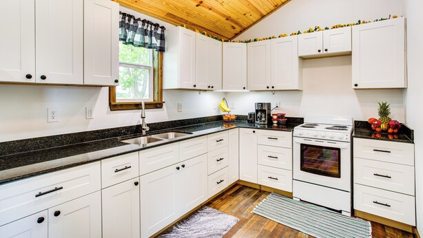 A kitchen with white cabinets, a black countertop, a wooden ceiling, and a window with a black and white curtain. - Northeast Texas Vacation Rental ~ 6 Mi to Commerce (Commerce)