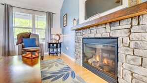 A living room with a stone fireplace, a sofa with a blue cushion, and a wooden coffee table. - Cozy Cottage in Taylorsville: Hot Tub & Lake Views (Taylorsville)
