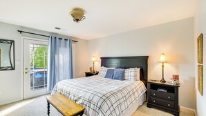 A bedroom with a bed, bedside tables, a bench, a door with a view, and a ceiling light fixture. - Cozy Cottage in Taylorsville: Hot Tub & Lake Views (Taylorsville)