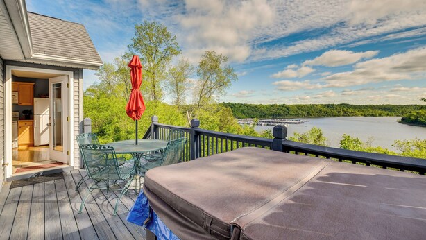 A deck with a table and chairs, a red umbrella, and a view of a lake and forest. - Cozy Cottage in Taylorsville: Hot Tub & Lake Views (Taylorsville)