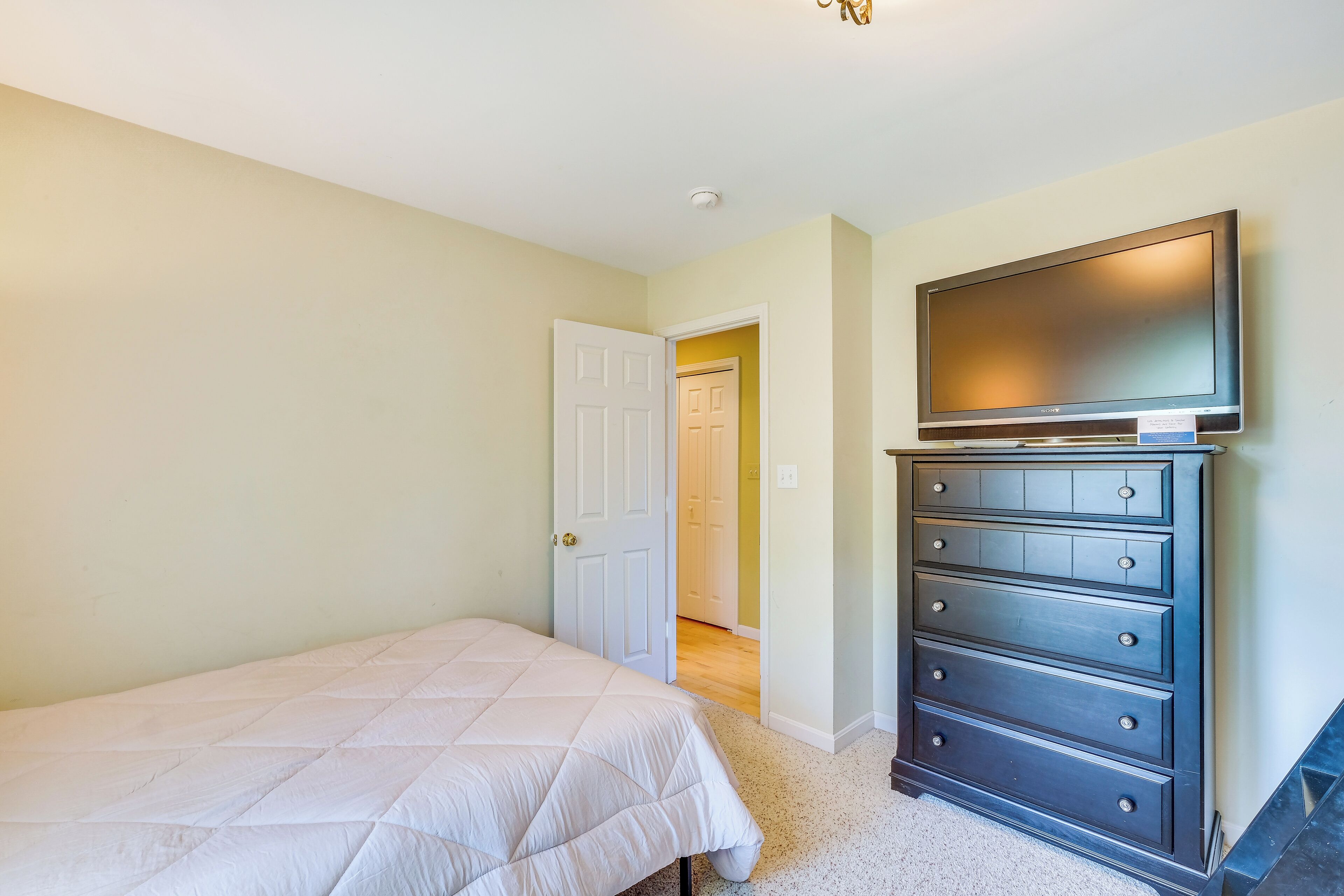 A bedroom with a bed, a dresser, and a television on the wall.