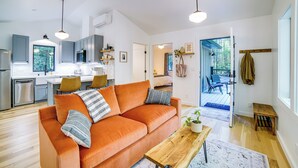 Un salon moderne avec un canapé, une table basse et un coin repas. On aperçoit une cuisine à l’arrière-plan, avec des placards et un réfrigérateur.