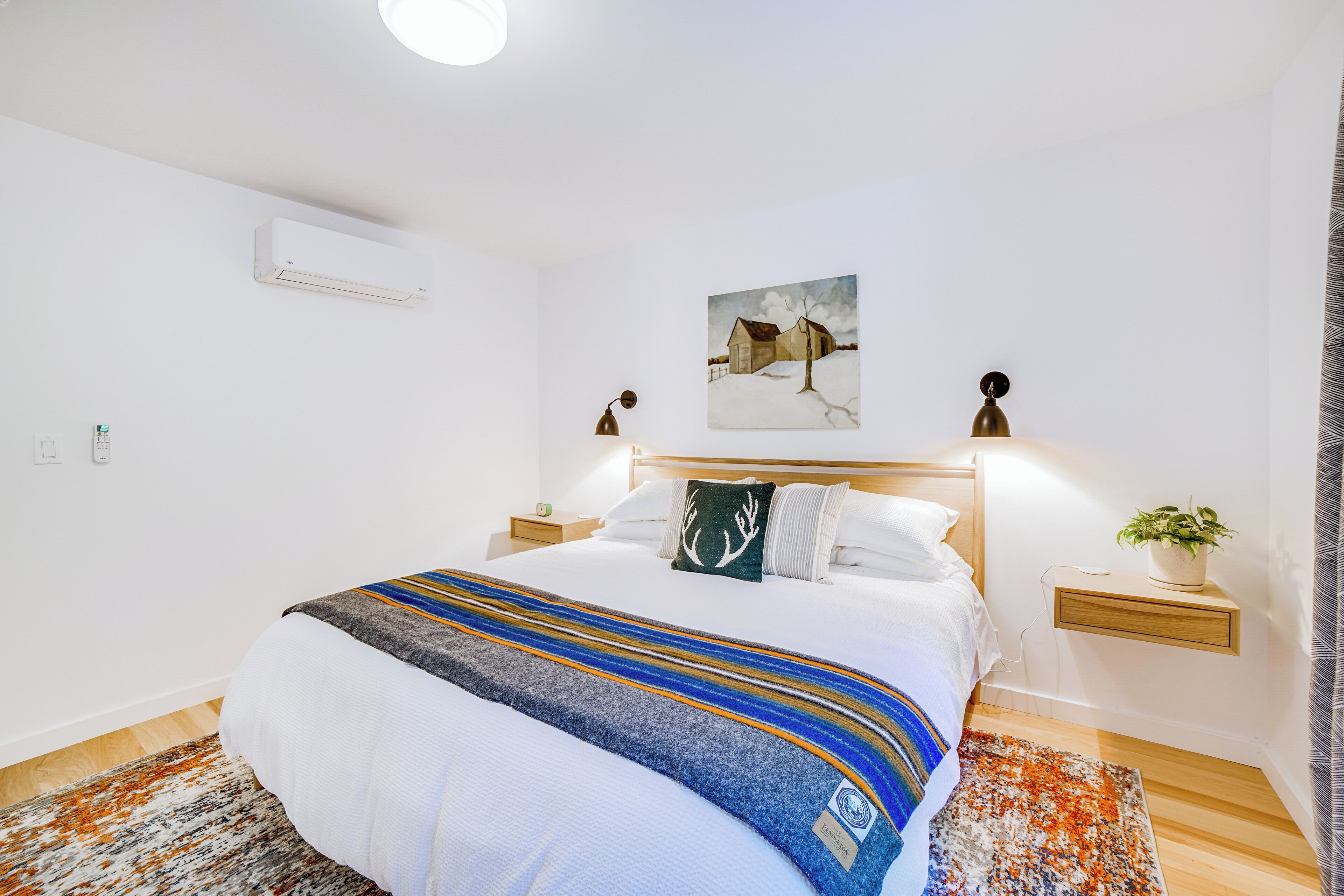 Un dormitorio ordenado con cama, mesitas de noche, aire acondicionado de pared y un cuadro.
