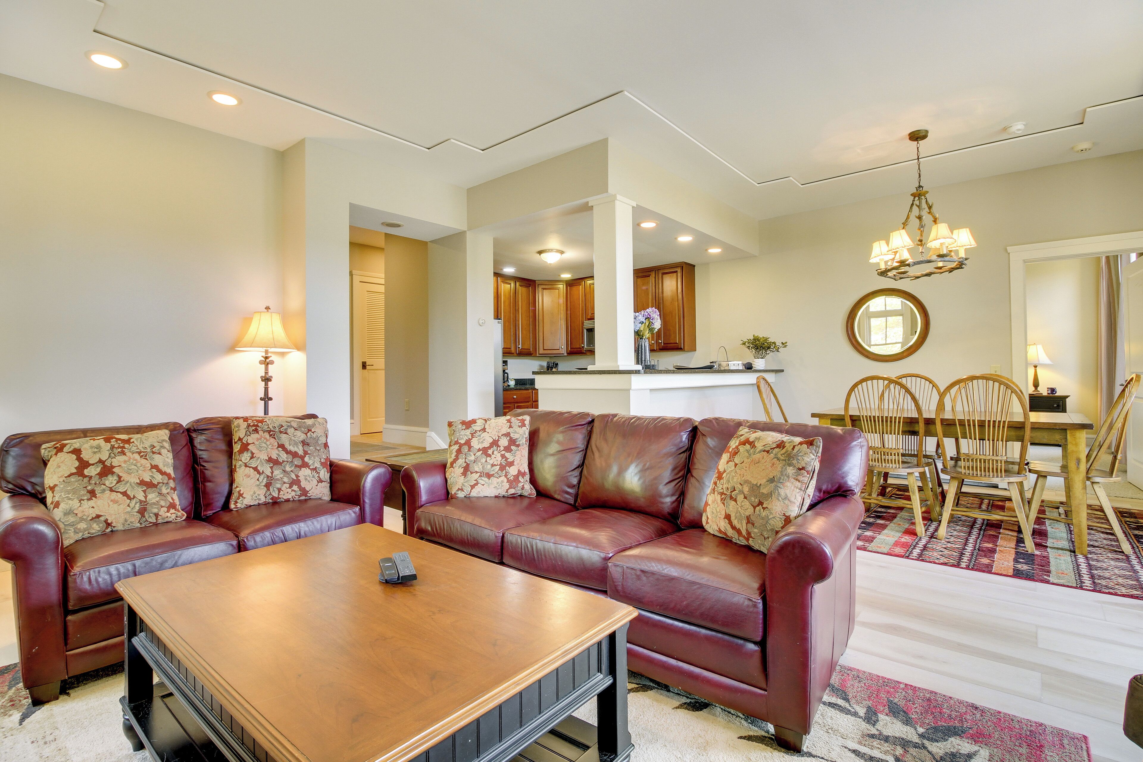 A living room with a brown leather sofa set, a wooden coffee table, and a dining area with a wooden table and chairs.