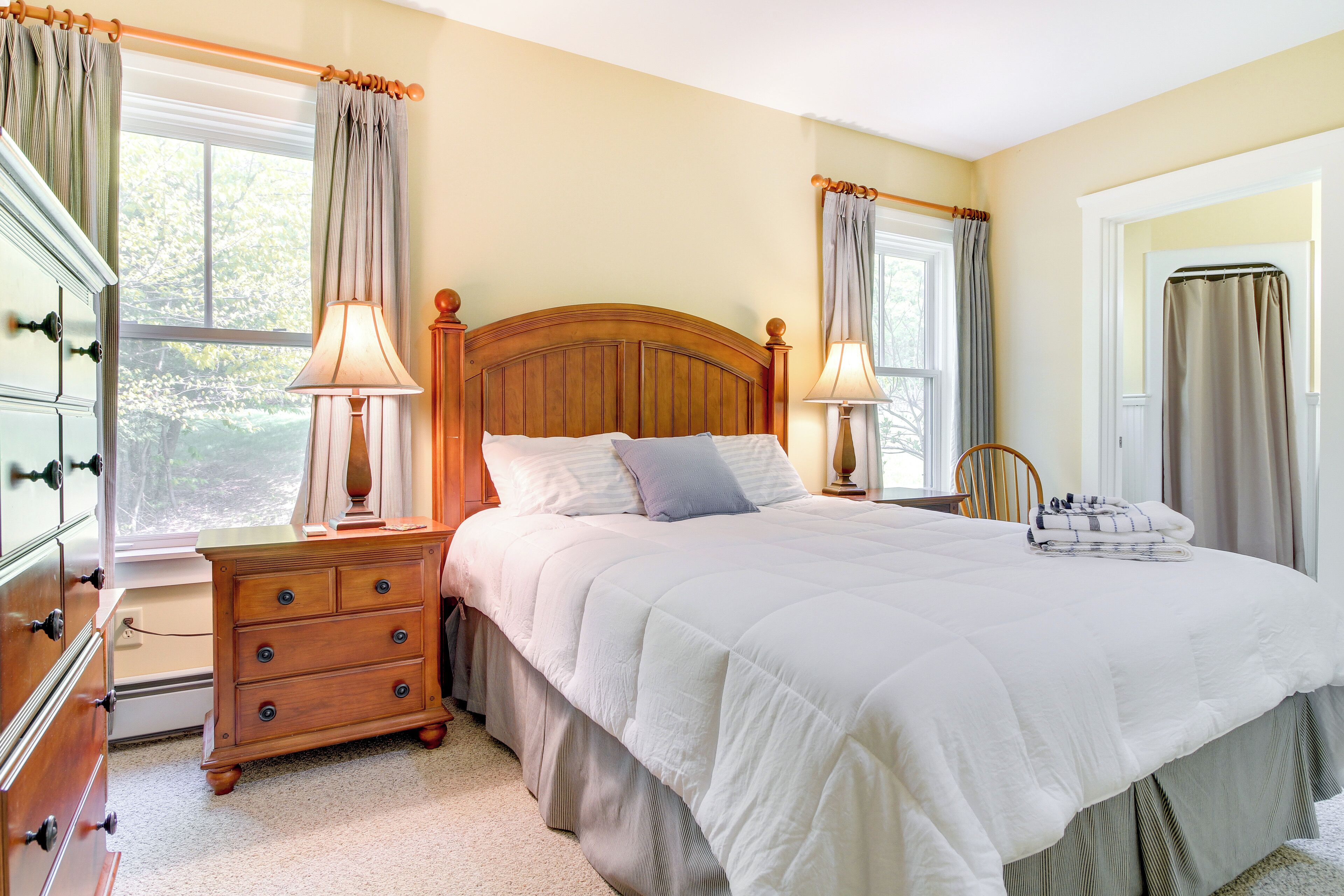A bedroom with a wooden bed, two bedside tables with lamps, a dresser, and a window with curtains.
