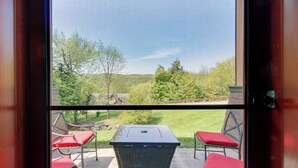 Une terrasse avec une table et des chaises, une porte-moustiquaire et une vue sur un espace verdoyant bordé d’arbres.