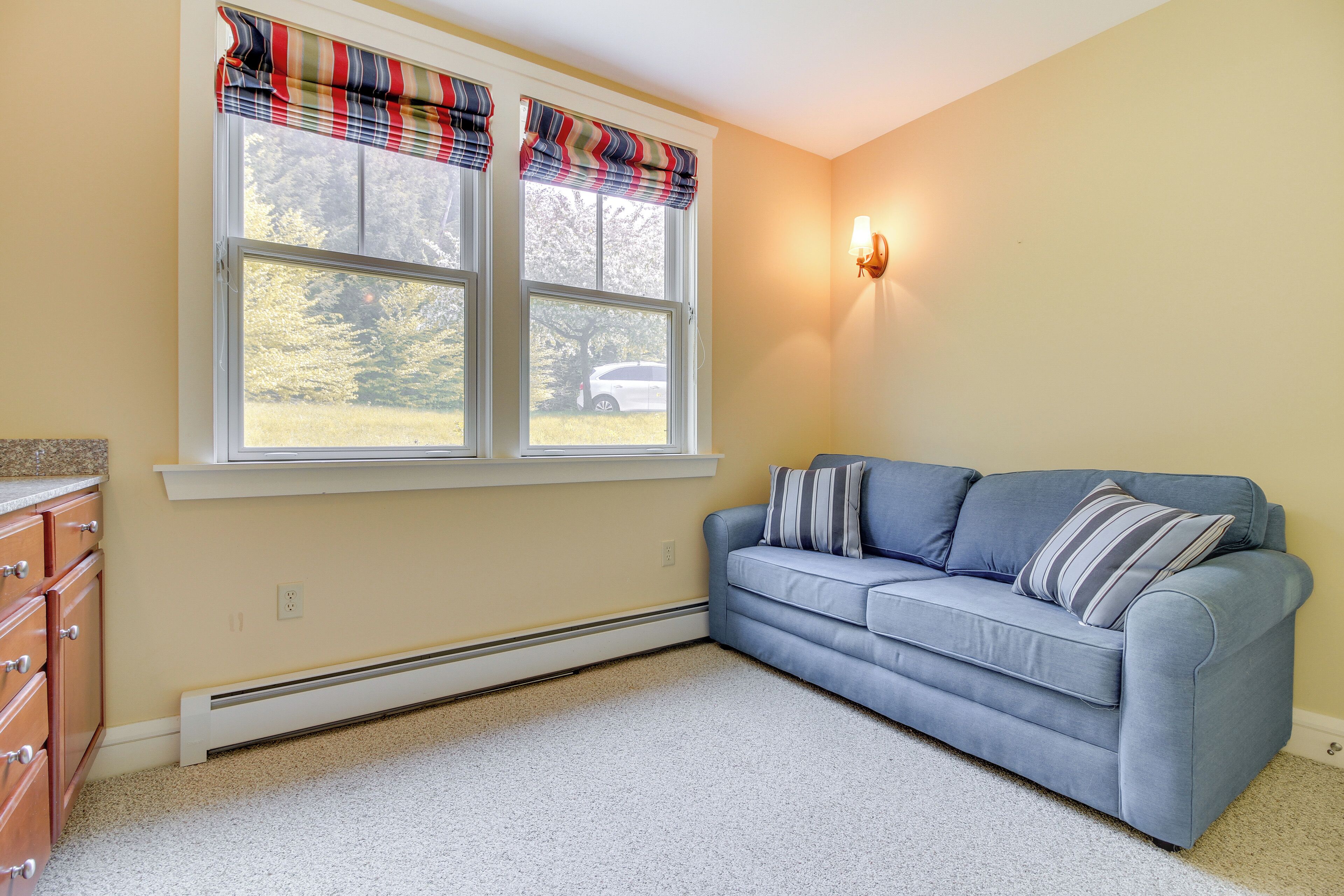 A room with a blue sofa, a window with plaid curtains, a wall-mounted light, and a white radiator.