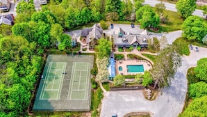 Vue aérienne d’une propriété résidentielle comprenant un court de tennis, une piscine et plusieurs maisons.