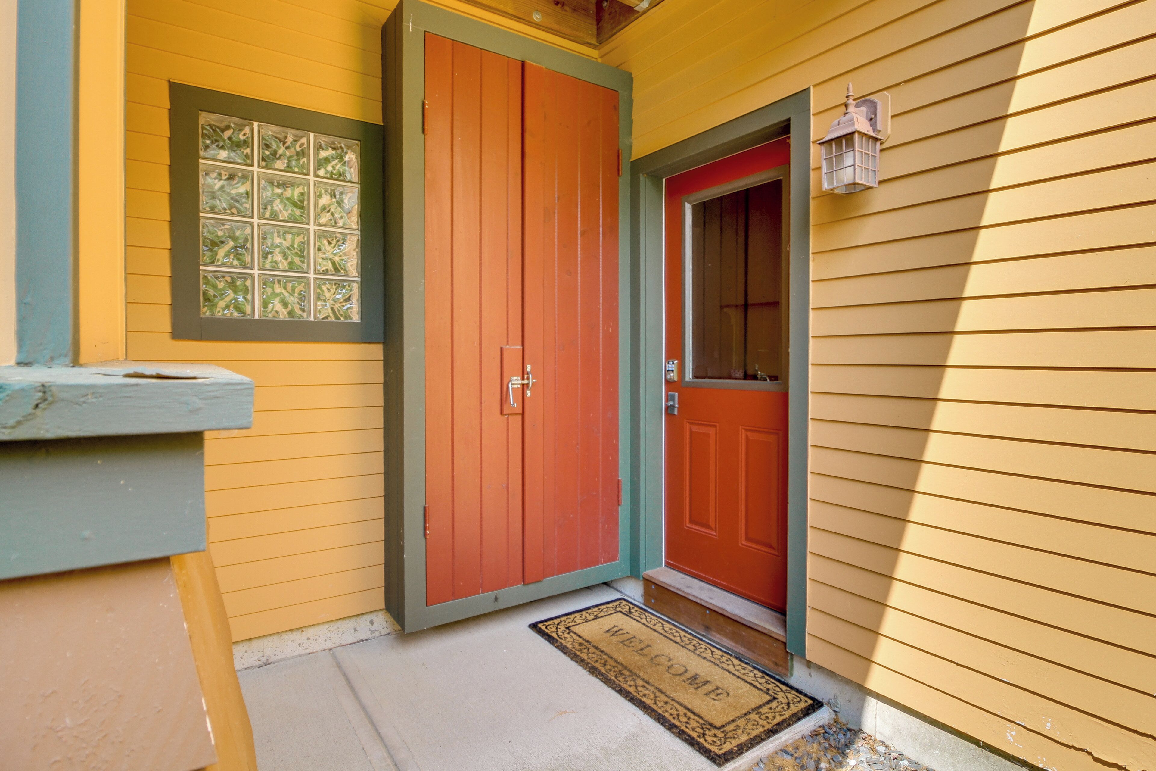 A yellow house with a red door and a window with a green frame.