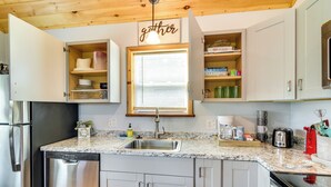 A kitchen with white cabinets, a stainless steel dishwasher, a granite countertop, and a window with blinds. - Cozy New York Abode - Porch, Near Fishing & Hiking (Jordan)