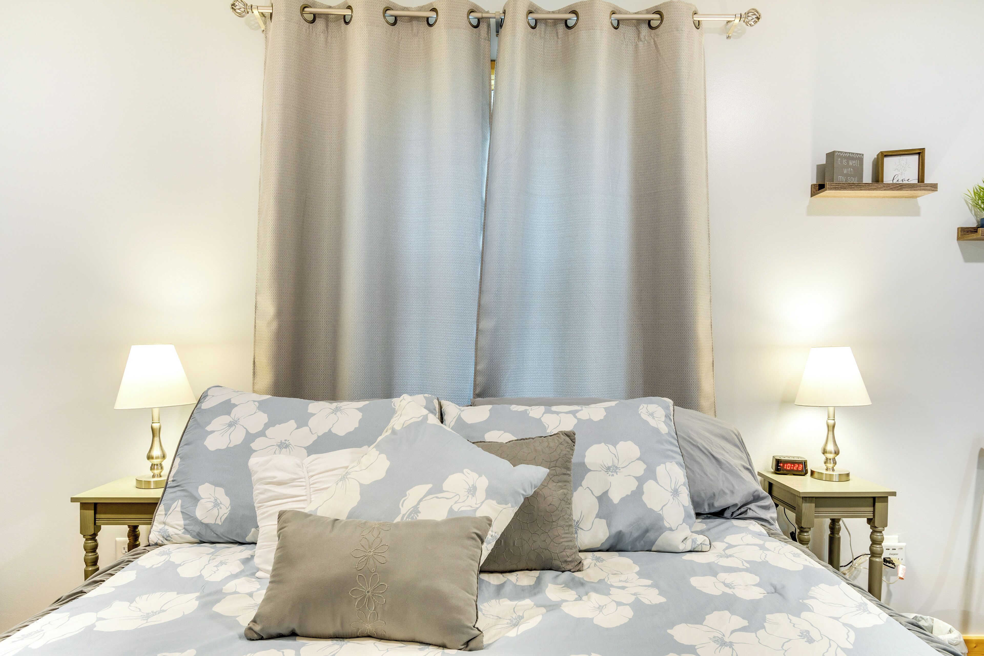 A neatly made bed with floral bedding, two bedside lamps, and a nightstand with a clock.
