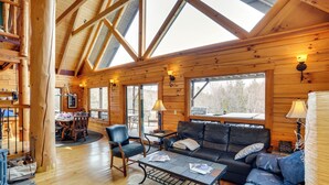A log cabin interior with a dining area, a sofa, and a fireplace. - Berkshire Hills Nature Lovers' Log Home Retreat (Windsor)