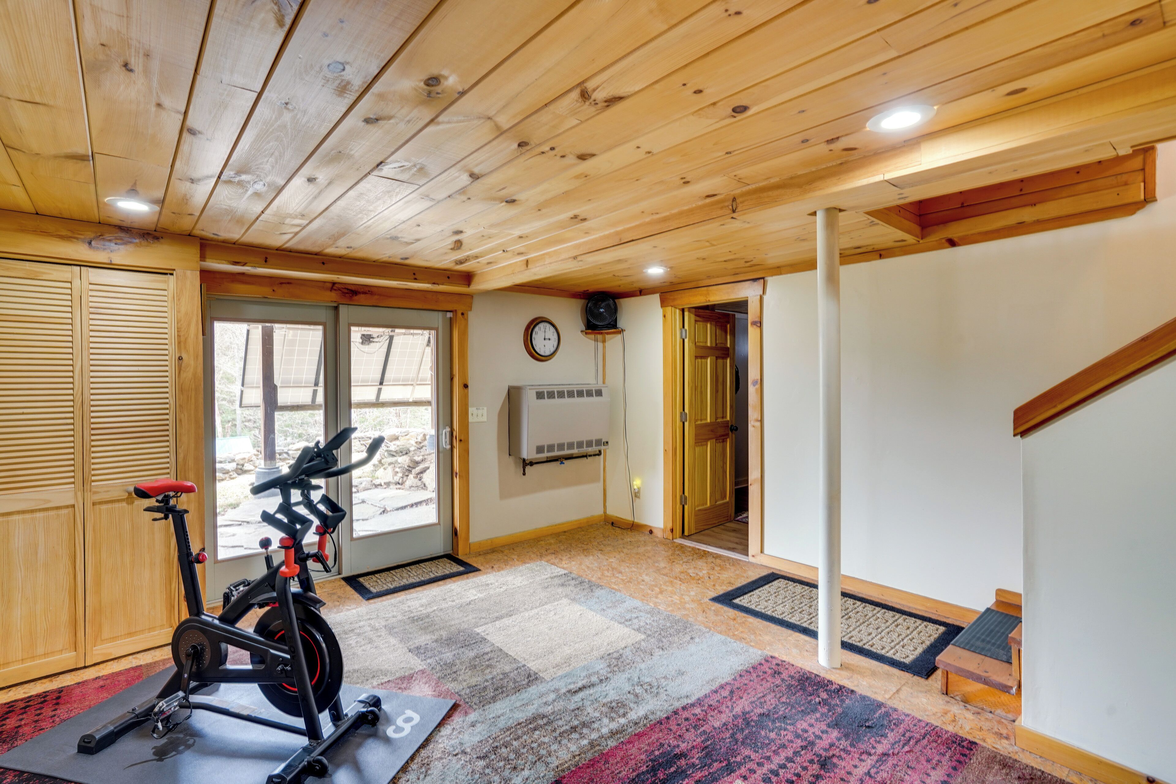 Une pièce équipée d’un vélo d’appartement, avec un plafond en bois et une porte donnant sur une autre pièce.