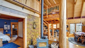 A rustic cabin interior with a stone fireplace, wooden beams, and a dining area. - Berkshire Hills Nature Lovers' Log Home Retreat (Windsor)