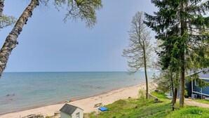 A beach view with a small cabin, a picnic table, and a blue tarp on the sand. - Beachy Palms Cottage on Lake Huron w/ Hot Tub! (Palms)