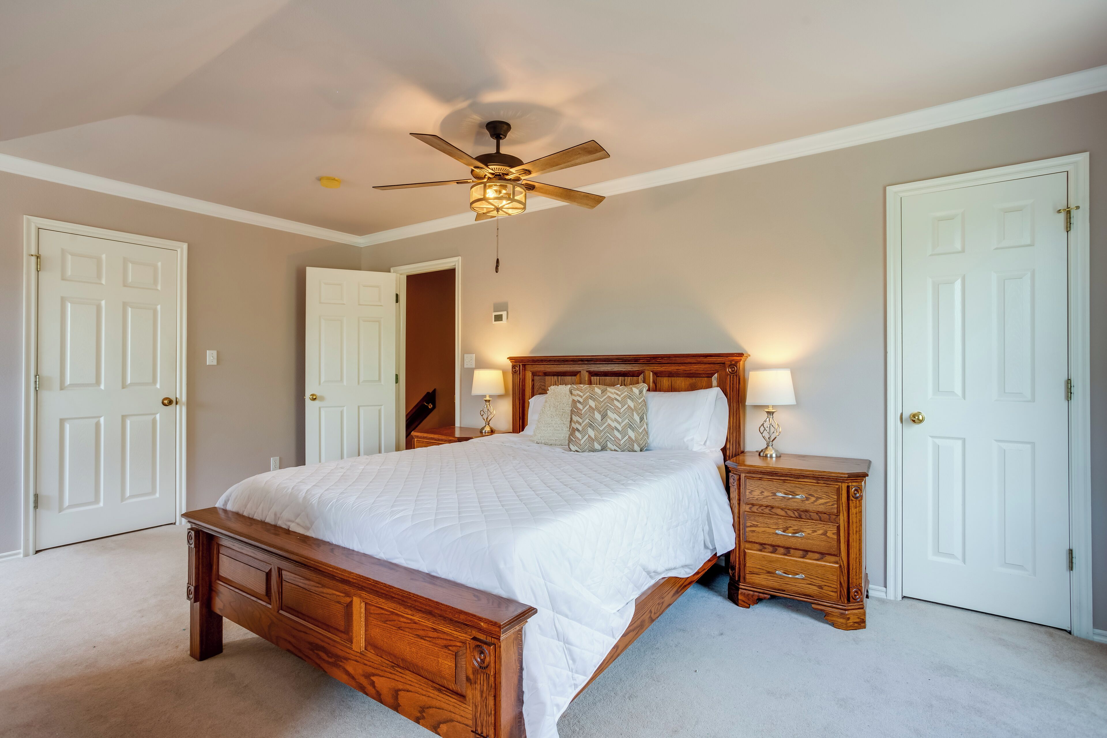 A bedroom with a wooden bed, a ceiling fan, and white doors.