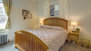 A bedroom with a wooden bed, two bedside lamps, a nightstand with a plant, and a radiator. - Walk to Restaurants & Shops: Apt in Pennsylvania! (Pottstown)