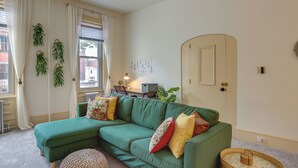 A green sectional sofa with multiple cushions, a wicker side table, and a small round ottoman. - Walk to Restaurants & Shops: Apt in Pennsylvania! (Pottstown)