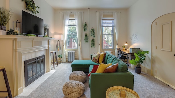 A living room with a fireplace, green sofa, ottomans, and a television. - Walk to Restaurants & Shops: Apt in Pennsylvania! (Pottstown)