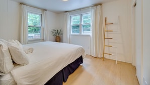 A bedroom with a large bed, two windows with curtains, a wooden ladder, and a plant on the windowsill. - Maryland Vacation Rental w/ Private Pool & Dock (Lusby)
