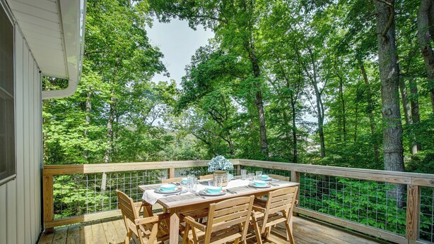 A wooden deck with a table set for dining, surrounded by trees. - Maryland Vacation Rental w/ Private Pool & Dock (Lusby)
