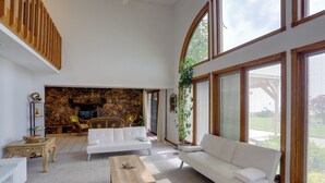 A spacious living room with a stone fireplace, white sofas, and large windows.