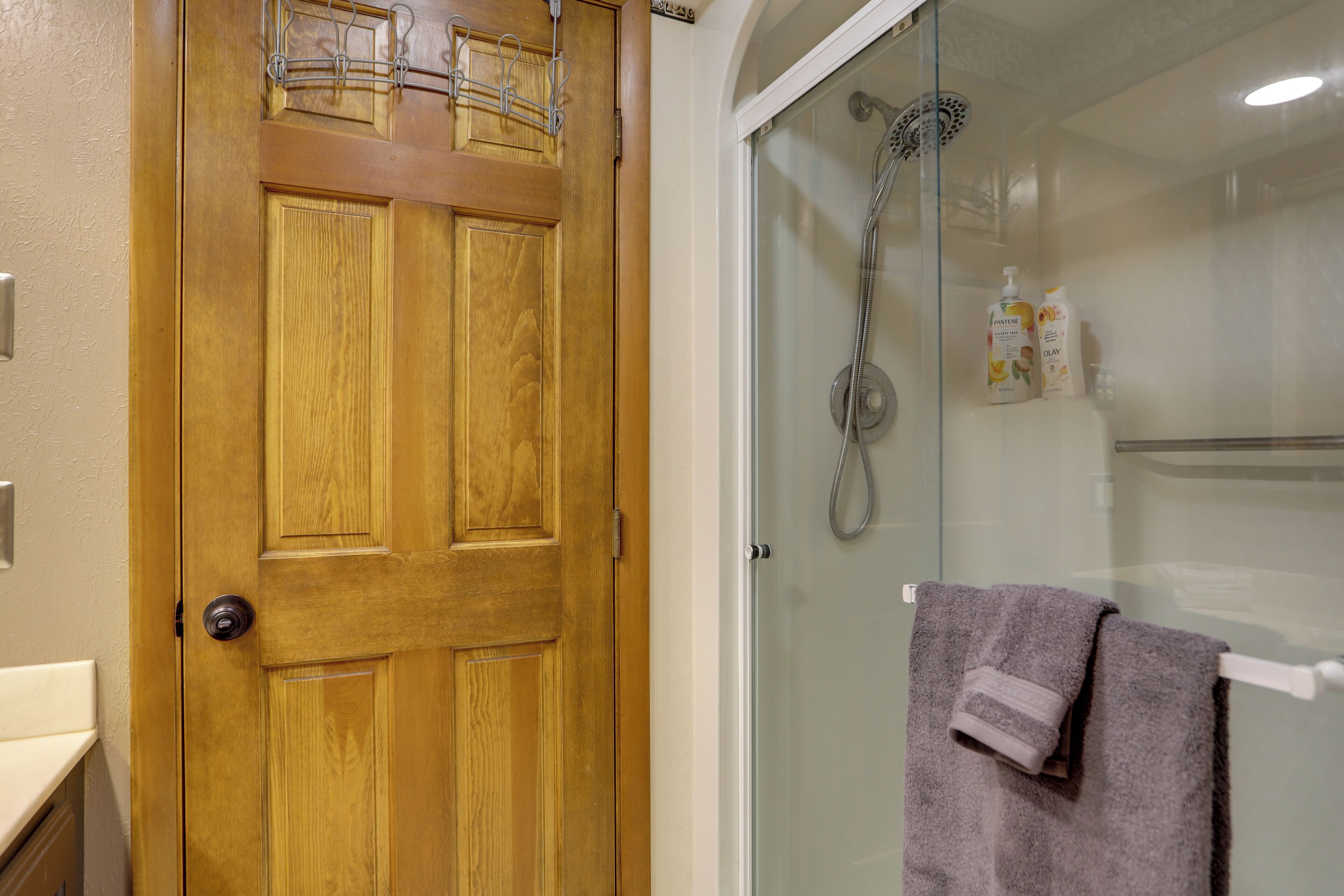Una porta in legno con maniglia in metallo e cabina doccia in vetro, con un asciugamano appeso a un porta-asciugamani.