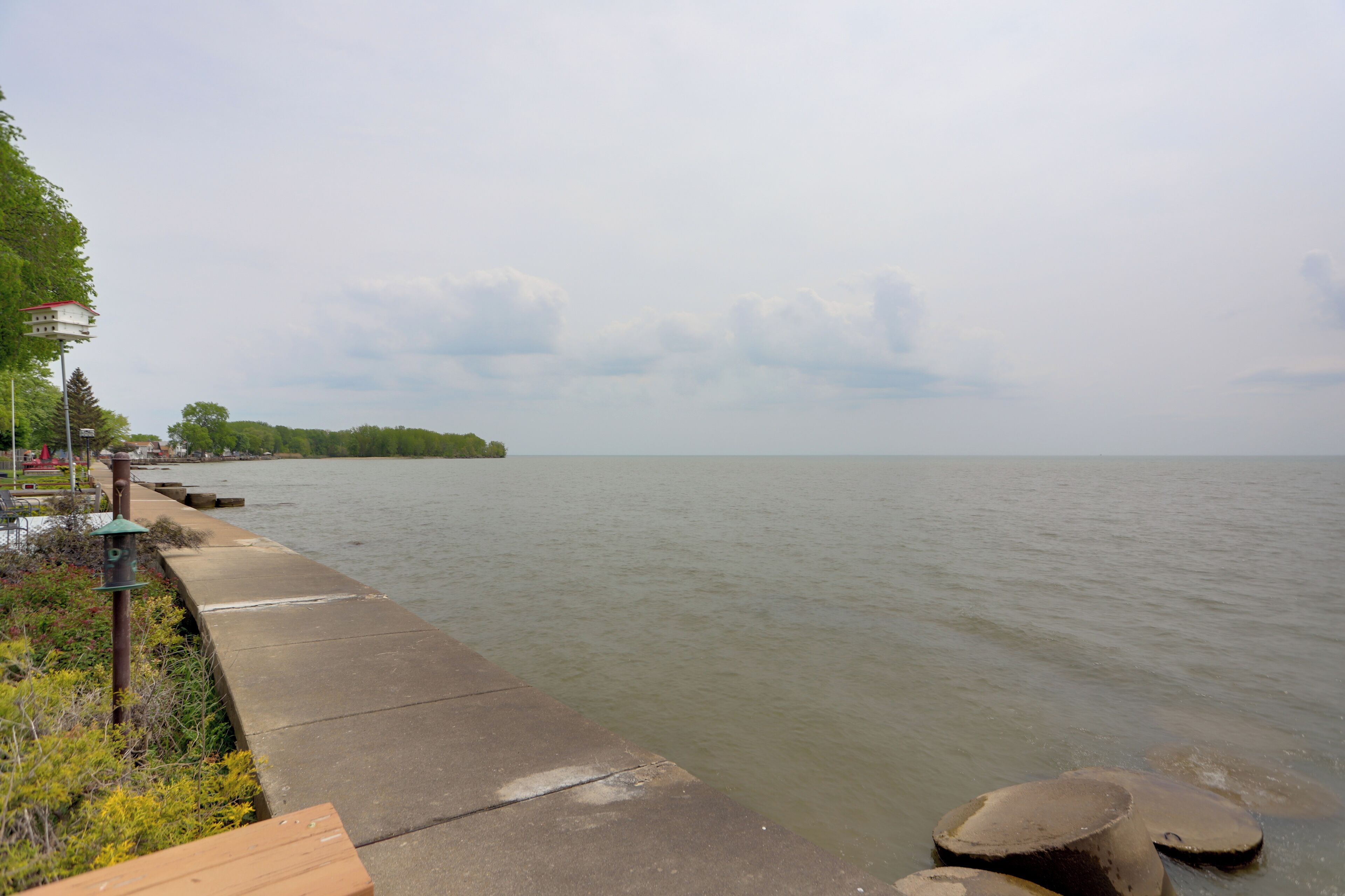 A concrete waterfront walkway with benches and a lamp post.