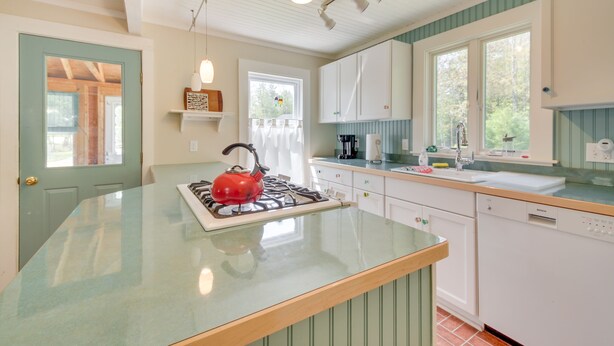 A kitchen with a central island, white cabinets, a red kettle, and a window with curtains. - Georgetown Vacation Rental: Gas Grill & Near Beach (Georgetown)
