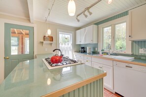 A kitchen with a central island, white cabinets, a red kettle, and a window with curtains. - Georgetown Vacation Rental: Gas Grill & Near Beach (Georgetown)