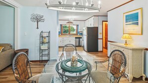 A dining area with a round glass table, wicker chairs, a chandelier, and a kitchen in the background. - 6 Mi to Beach: Myrtle Beach Escape w/ Sunroom! (Myrtle Beach)