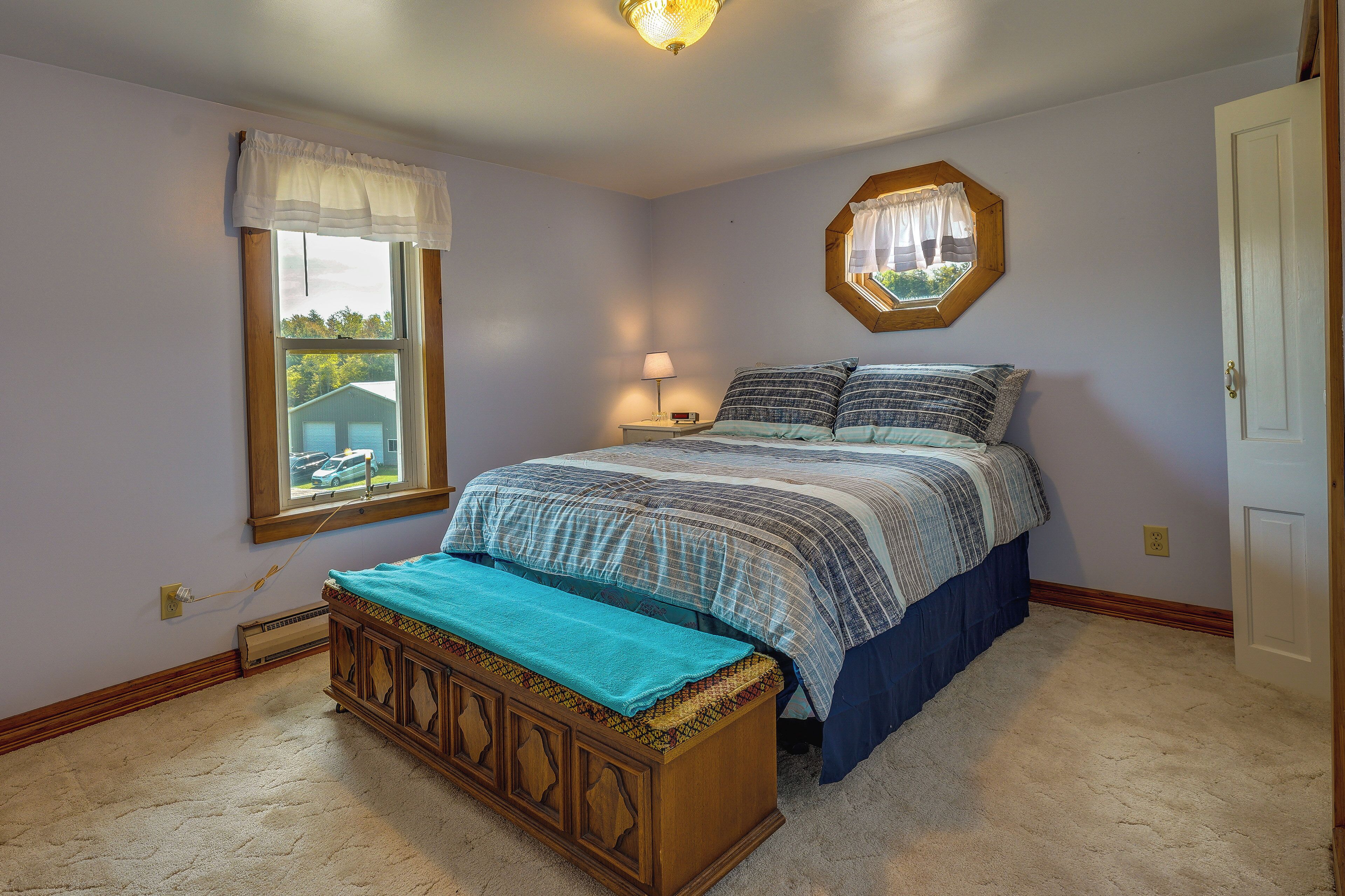 A bedroom with a bed, a bench, a window, a nightstand, and a mirror.