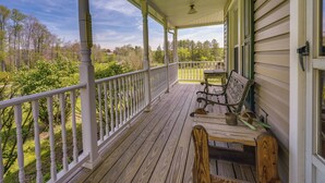A covered porch with a wooden bench and a table, overlooking a green landscape. - Spacious Pennsylvania Vacation Rental w/ Backyard (Kersey)