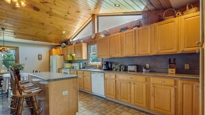A kitchen with wooden cabinets, a central island, bar stools, and a view of the outdoors. - Spacious Pennsylvania Vacation Rental w/ Backyard (Kersey)