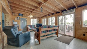 Ein Holzblockhaus-Innenraum mit einer Couch, einem Relaxsessel, einem Fernseher und einem großen Fenster.