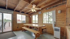 Eine Holzhütte mit einem großen Tisch, Bänken, einem Deckenventilator und einer Heizung.
