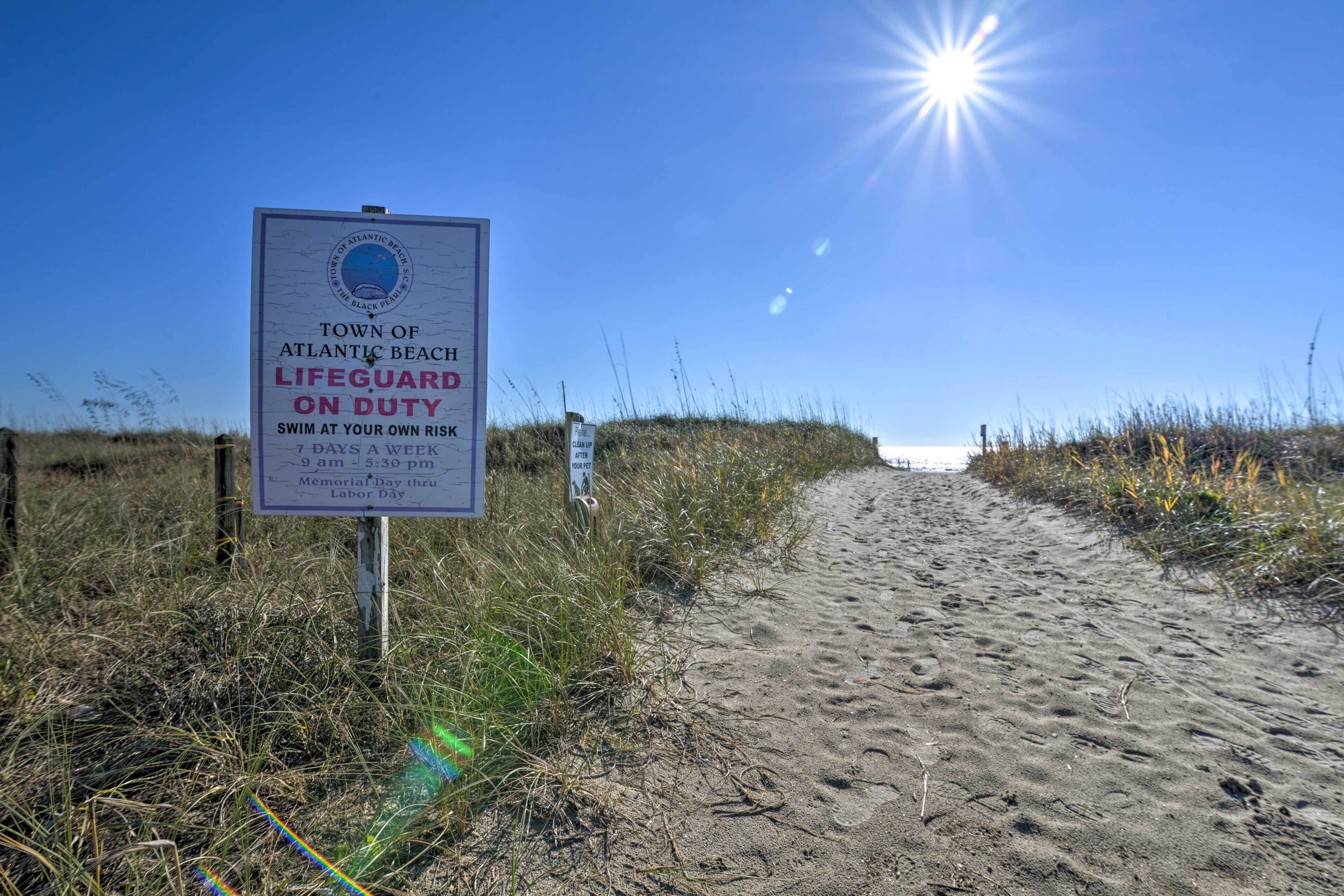 Ein Strandweg mit einem Rettungsschwimmer-Schild und einer Sonne im Hintergrund.