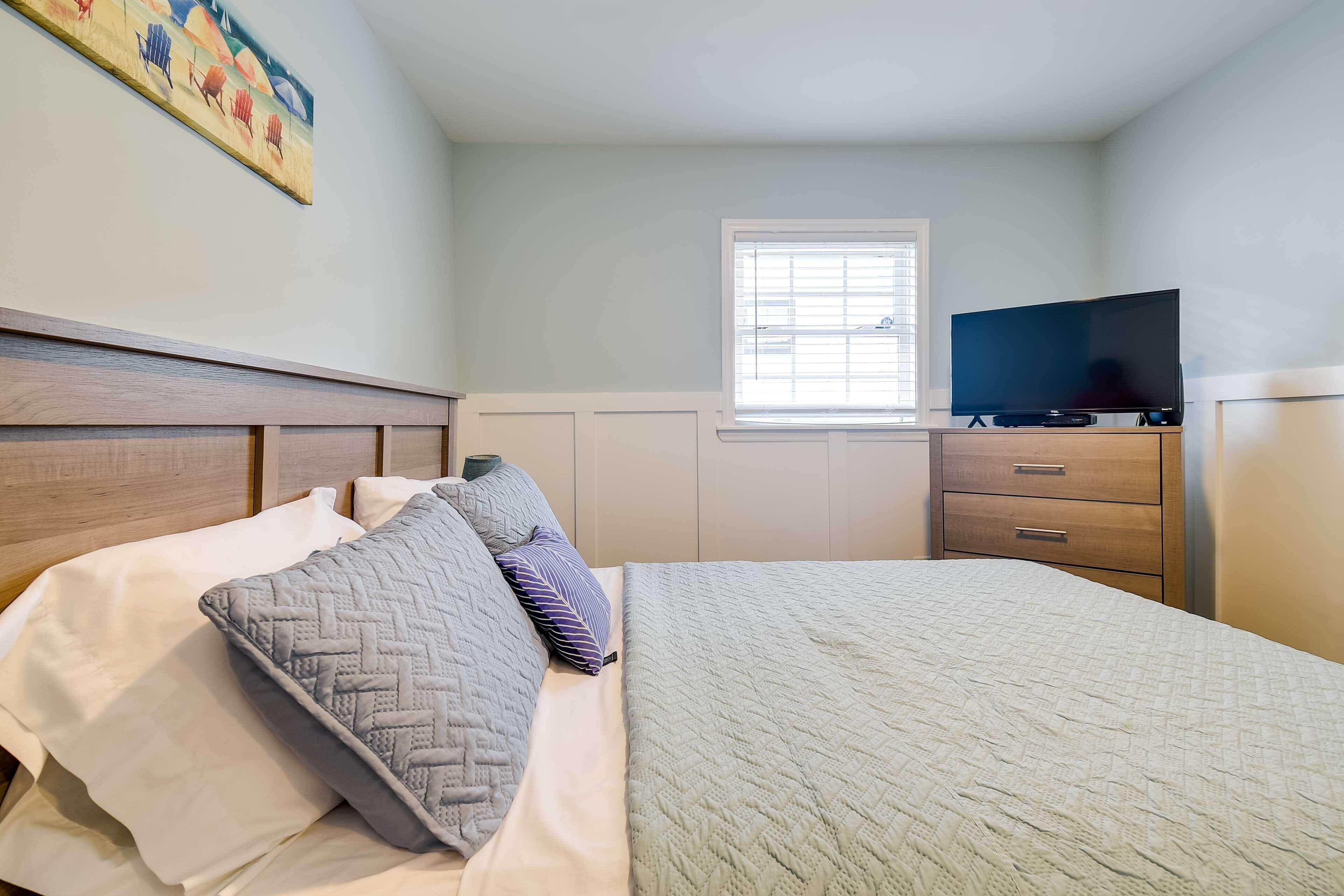 A bedroom with a bed, a television on a stand, a window, and a dresser.