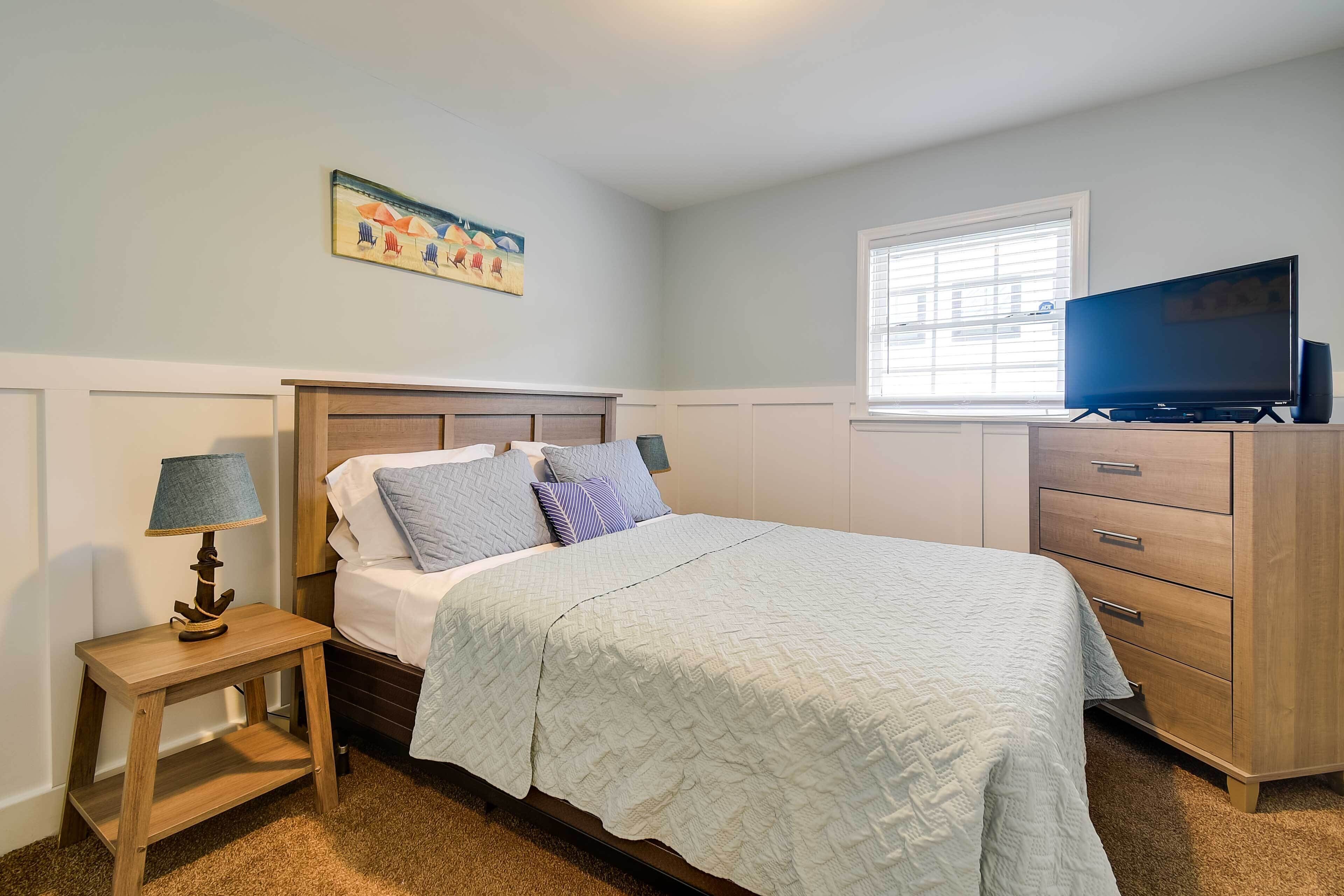 A bedroom with a bed, a nightstand, a dresser, a television, and a window with blinds.