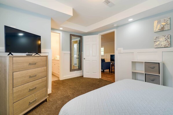 A bedroom with a bed, a TV on a dresser, a door leading to another room, and a wall with artwork.