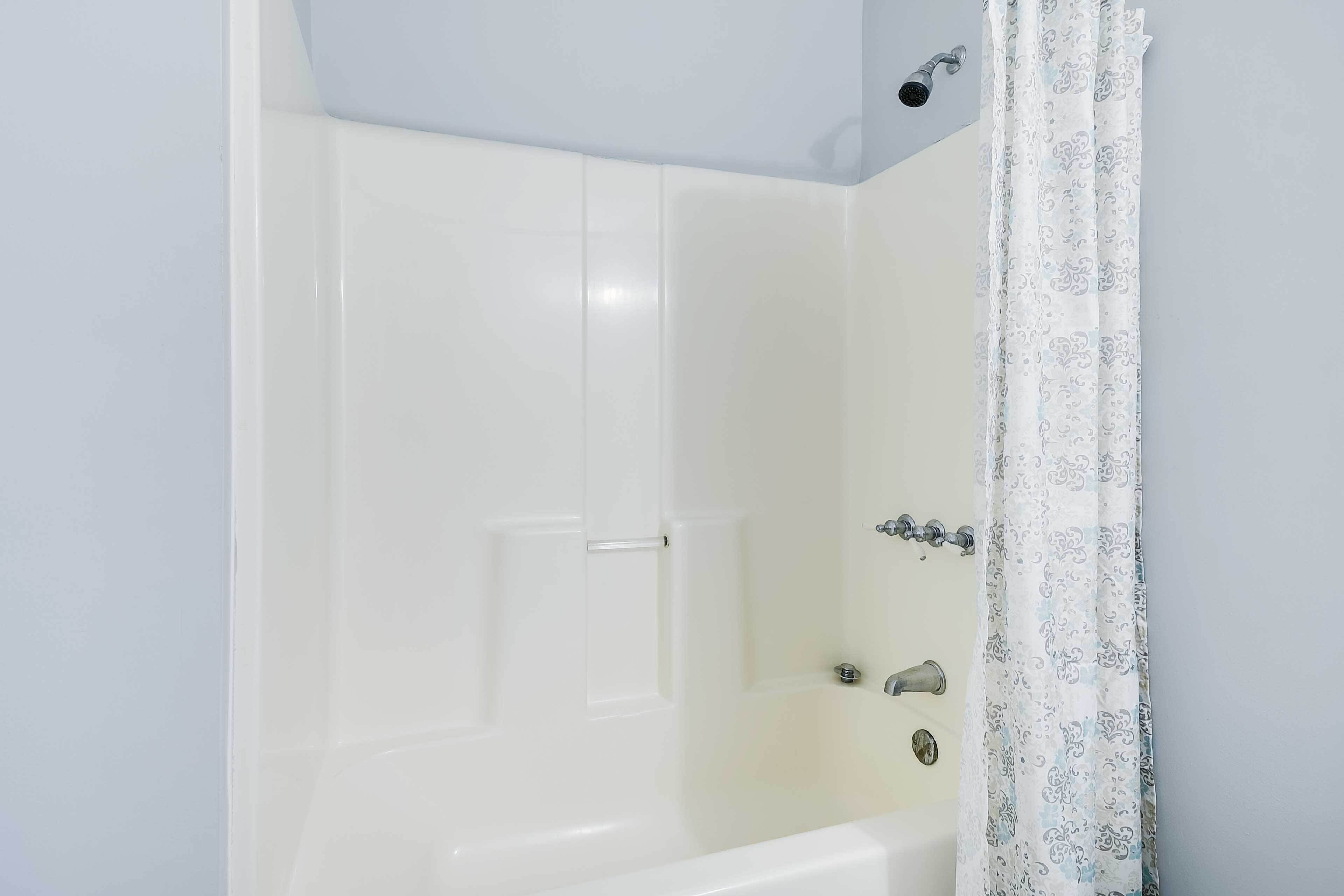 A white bathtub with a showerhead and a curtain.