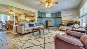 A spacious living room with a ceiling fan, a dining area with chairs, a kitchen in the background, and a large window providing natural light. - Delaware Vacation Rental: Walk to Lake Dardanelle! (Delaware)