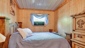A wooden-paneled room with a bed, a dresser, and a window with curtains. - Stargaze, Hike & Kayak: Cabin Near Copper Breaks! (Crowell)