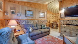A cozy living room with a sofa, armchairs, a stone fireplace, wooden walls, and a flat-screen TV. - Stargaze, Hike & Kayak: Cabin Near Copper Breaks! (Crowell)