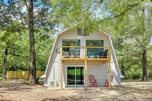 A two-story cabin with a balcony, large windows, and a sliding glass door. - Family-friendly Broken Bow Home w/ Grill! (Broken Bow)