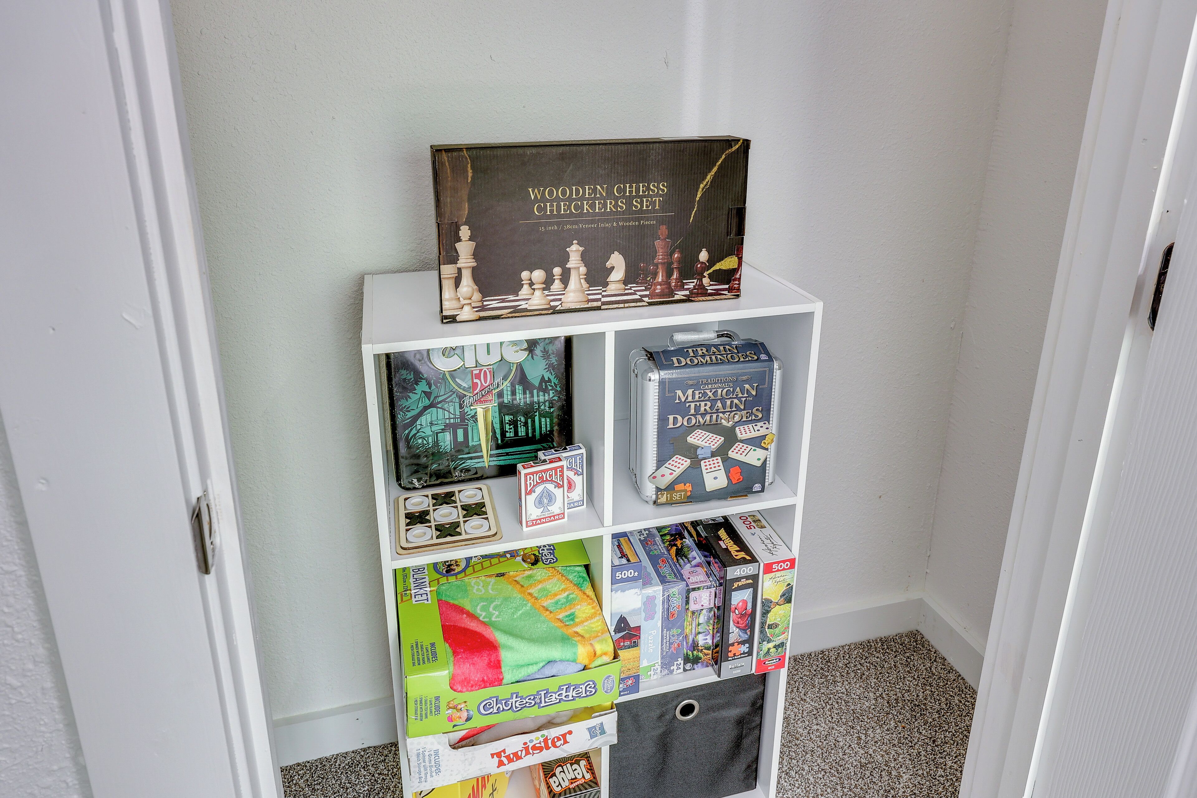A white shelf with various board games and a wooden chess checkers set.
