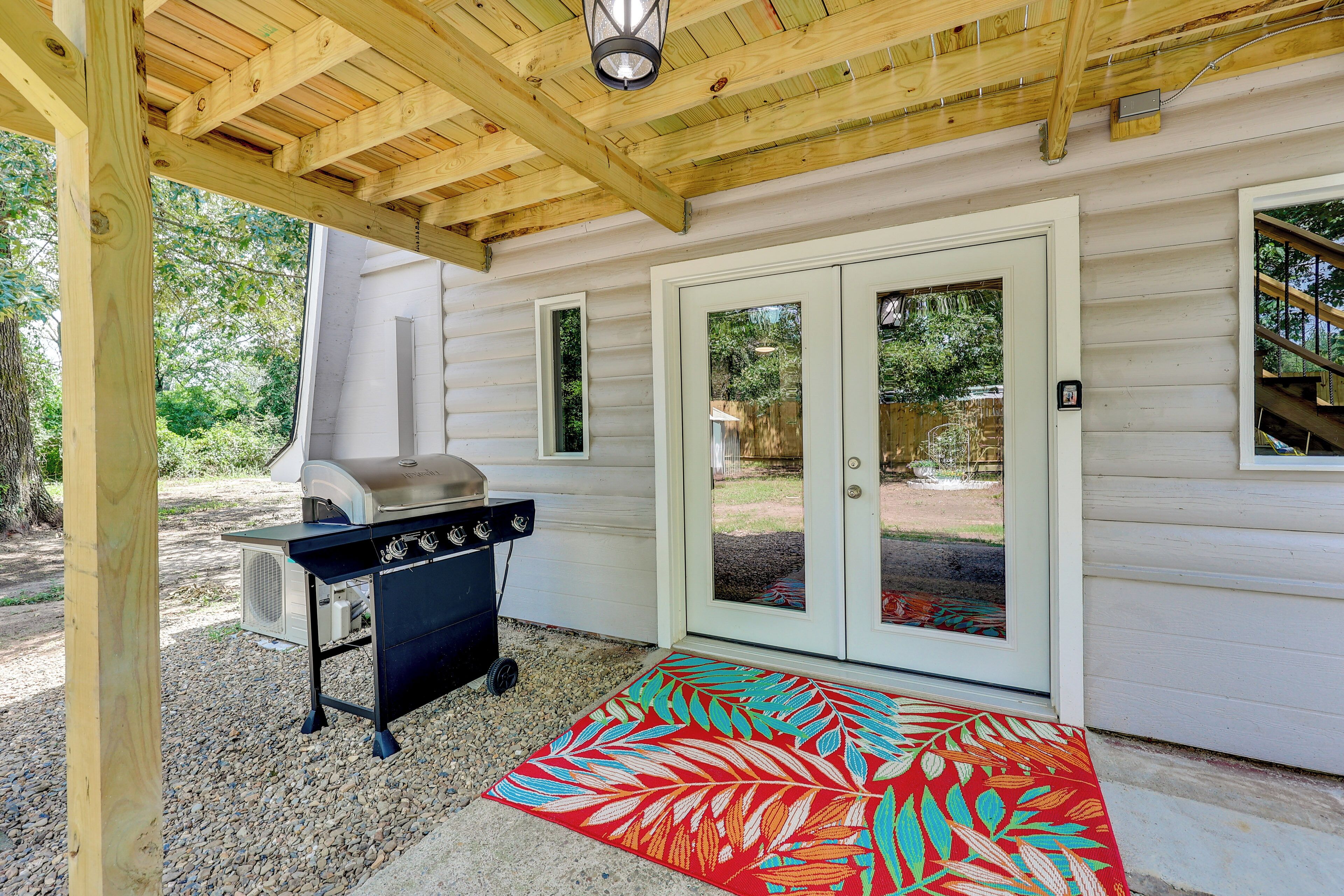A covered outdoor area with a grill, a red patterned mat, and a white door with glass panels.