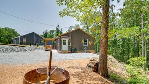 Une cabane rustique avec une allée en gravier, un barbecue en bois et un grand pot en métal.