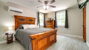 Une chambre avec un lit en bois, un ventilateur de plafond, un climatiseur et une commode.